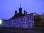 Келейный корпус с внешней стороны скита с примыкающей к нему монастырской стеной в сумерах. Над корпусом видны купола Черниговского храма