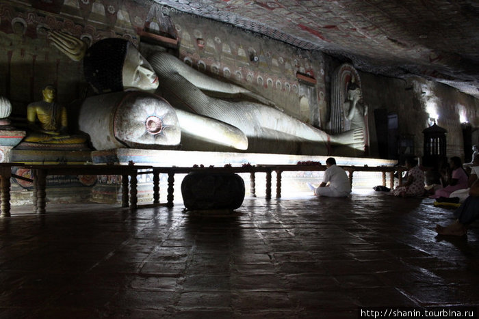 Монах и лежащий Будда в темноте пещеры Дамбулла, Шри-Ланка