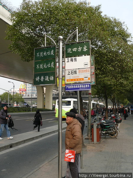 К столбикам прикручены обозначения проходящих мимо маршрутов. На зелёных табличка написано: «Не плеваться». «Говорить на Путунхуа». «Рады приветствовать гостей со всех четырёх сторон света!» Шанхай, Китай