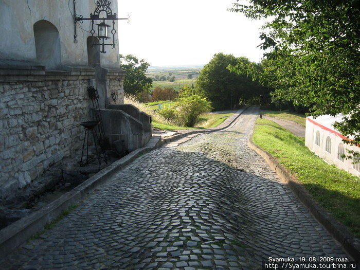 Неровная брусчатая дорожка и рядом с ней тротуар из неровно уложенных каменных плит вели к воротам замка. Олесько, Украина