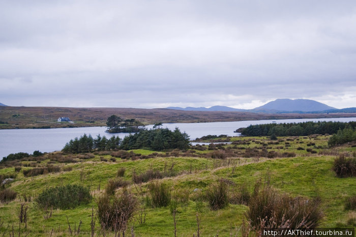 Озеро в долине между гор, облака, наползающие на их вершины, изумрудная трава и синее небо — вот, что такое это место Графство Голуэй, Ирландия