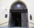 Массивная дверь с полуколоннами и красивым резным деревянным сводом является главным входом в костел.