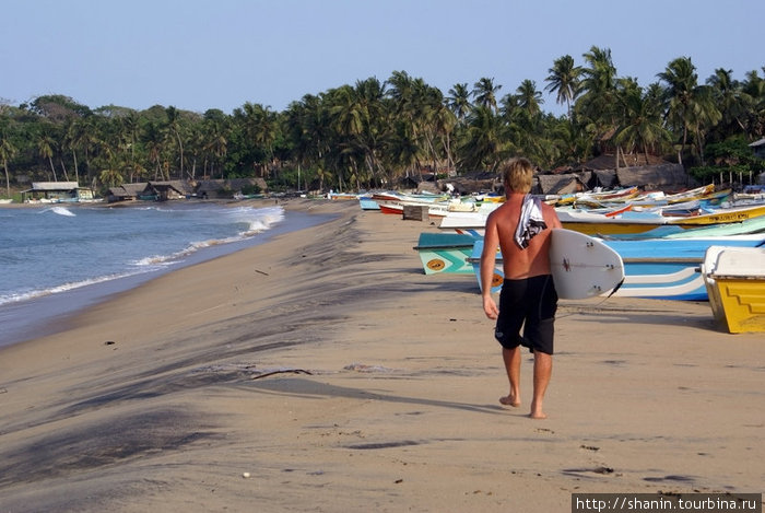 Серфер прогуливается по пляжу Аругам, Шри-Ланка