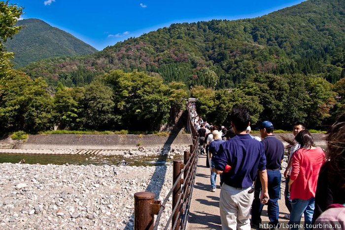 Толпы переправляются через реку Сё-гава от остановки в деревню Огимати, Япония