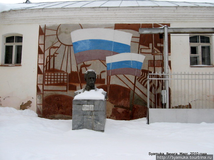 Перед проходной на фоне жизнеутверждающего панно, в снегу — бюст В. Ногина, установленный в годы Советской власти, по случаю присвоения фабрике его имени. Вичуга, Россия
