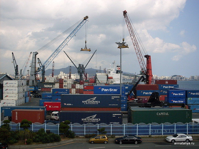 Грузовые краны и корабли, на которые вовсю идет погрузка огромных контейнеров с товарами Пусан, Республика Корея